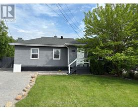 A grey house with a white fence and a tree in front.