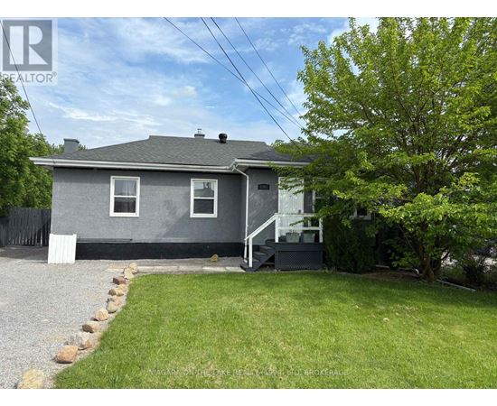 A grey house with a white fence and a tree in front.