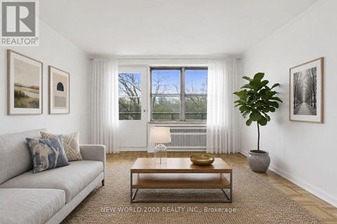 A living room with a grey couch, a coffee table, and a large window with white curtains.