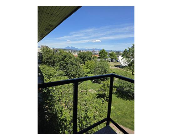 A balcony overlooks a lush green yard and distant mountains.