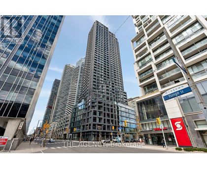 A tall building with a glass facade stands in front of a street with other buildings.
