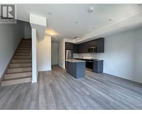 A spacious kitchen and living room with wood flooring and a staircase.