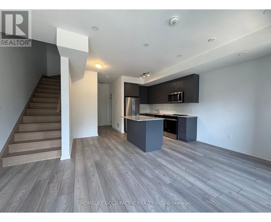A spacious kitchen and living room with wood flooring and a staircase.