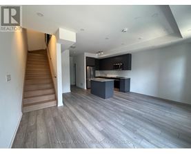A spacious living room with a staircase on the left and a kitchen area on the right.