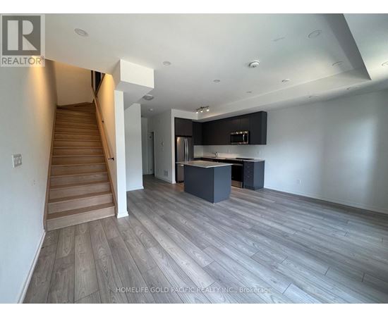 A spacious living room with a staircase on the left and a kitchen area on the right.