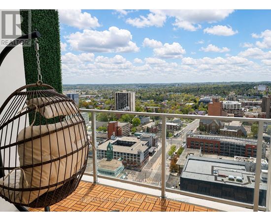 A birdcage is hanging from a chain on a balcony overlooking a cityscape.