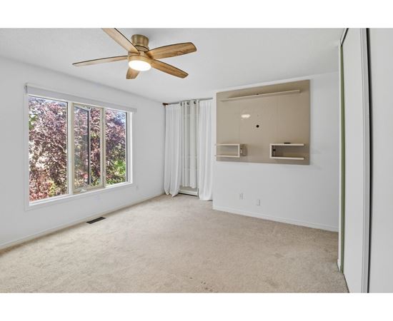 A room with a ceiling fan and a window overlooking trees.