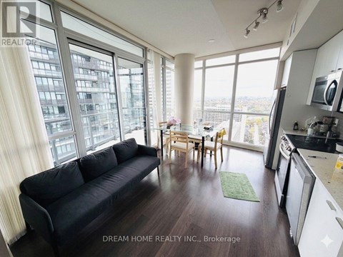 A black couch sits in a bright living room with a dining table and chairs in the background.