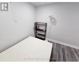 A white bed in a room with a small shelf and a lamp.