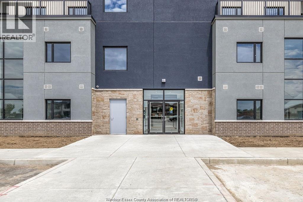 The image shows the front of a building with a grey and black facade, a glass door entrance, and a brick base.