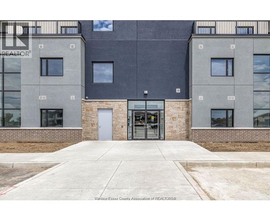 The image shows the front of a building with a grey and black facade, a glass door entrance, and a brick base.