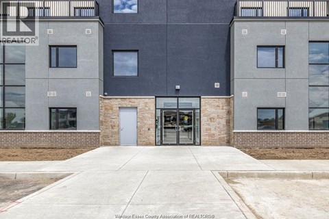 The image shows the front of a building with a grey and black facade, a glass door entrance, and a brick base.