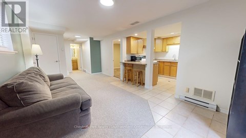 A living room with a grey couch and a kitchen area in the background.