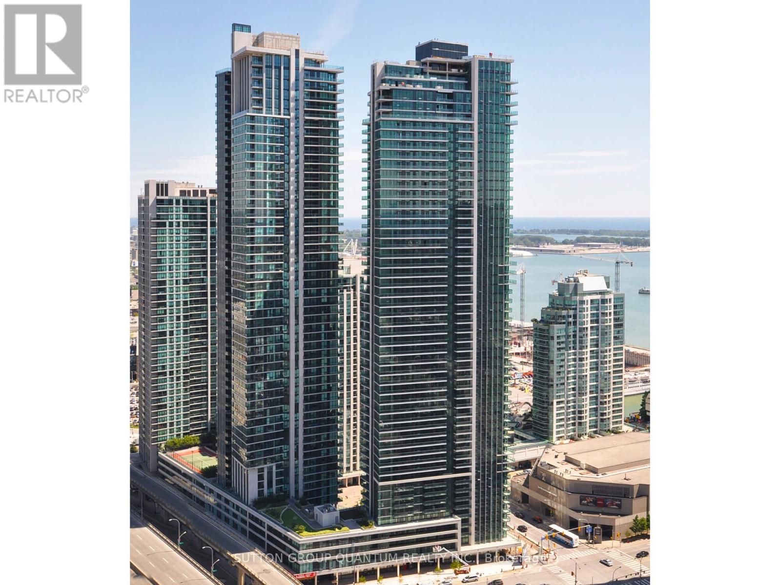 Two tall buildings stand next to each other with a body of water in the background.