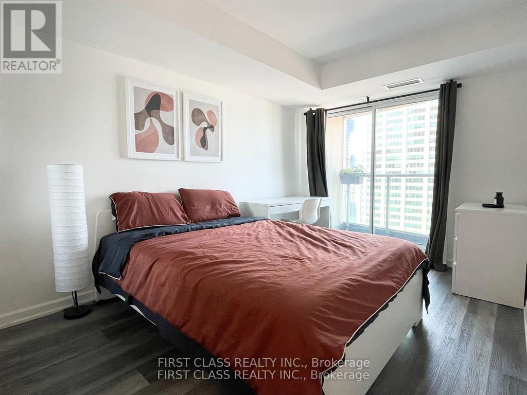 A bedroom with a red bedspread and a white nightstand.