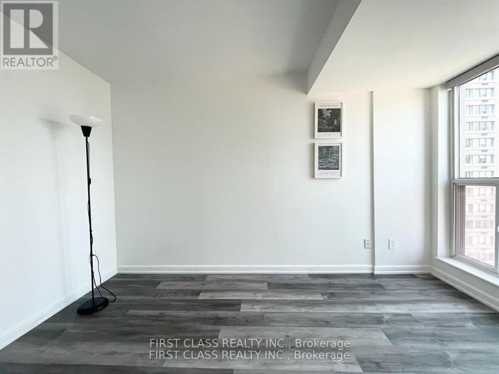 A room with a grey floor and a white wall with a picture frame and a lamp.