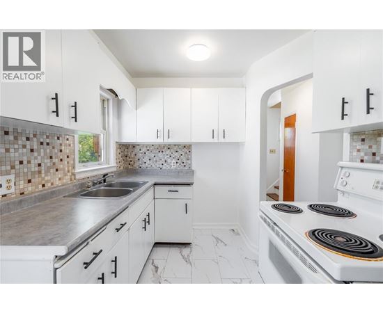 A white kitchen with a stove top oven and a sink.