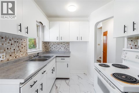 A white kitchen with a stove top oven and a sink.