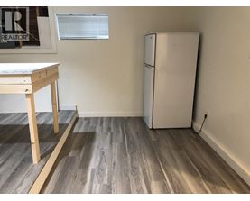 A white refrigerator sits next to a wooden table in a room with wooden flooring.