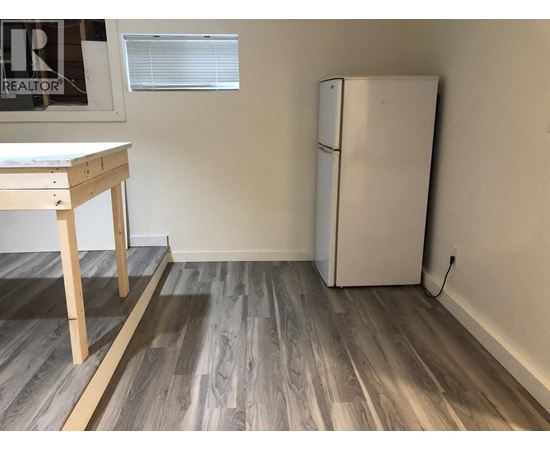 A white refrigerator sits next to a wooden table in a room with wooden flooring.