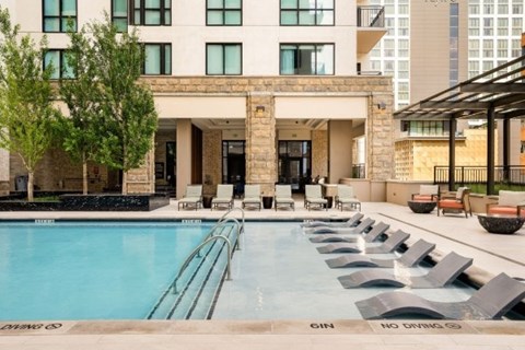 A large swimming pool with lounge chairs and a building in the background.