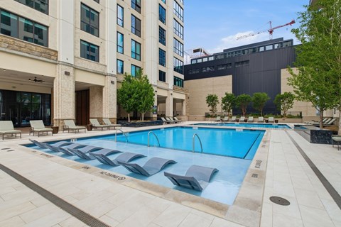 A large swimming pool with lounge chairs is surrounded by a building.