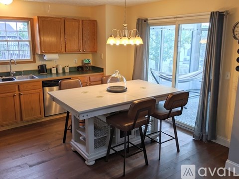 A kitchen with a table and chairs in the foreground and a window with a view of a balcony in the background.