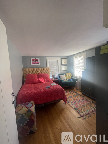 A bedroom with a red bedspread and a floral armchair.
