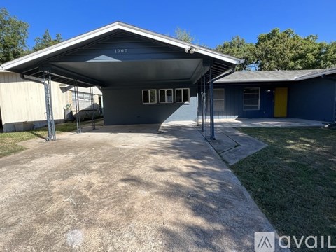 A blue building with a yellow door is surrounded by a gravel driveway.