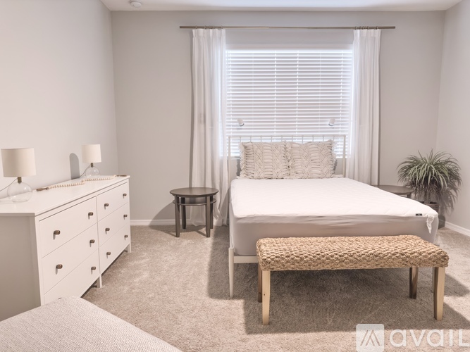 A bedroom with a white bed, a white dresser, and a white nightstand.
