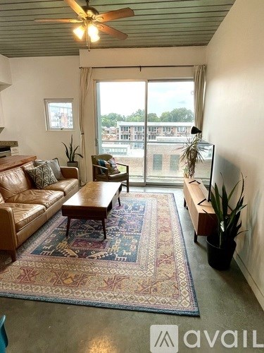 A living room with a brown leather couch, a rug, and a ceiling fan.