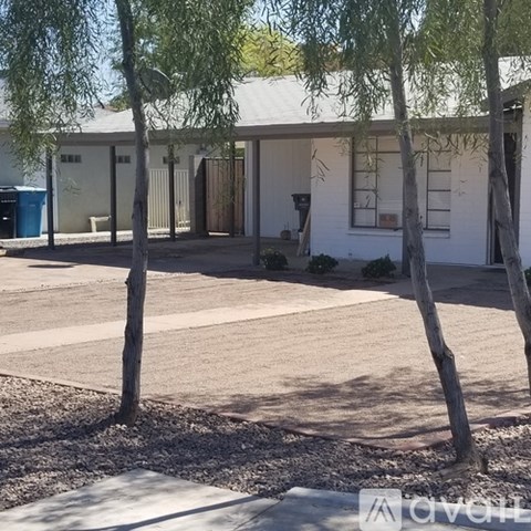 A white building with a porch and trees in front.