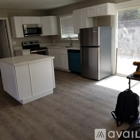 A kitchen with white cabinets and a black backpack on the floor.