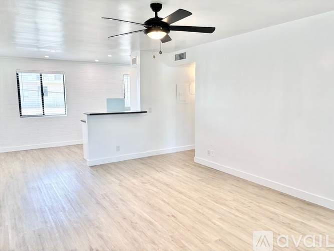 A spacious room with a ceiling fan and light, a window with blinds, and a white cabinet with a countertop.