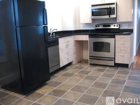 A black refrigerator is in a kitchen with a black counter top.