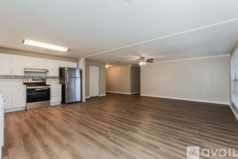 A spacious room with wooden flooring and a kitchen area with white cabinets and appliances.