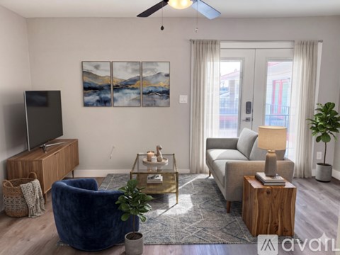 A living room with a blue chair, a sofa, a coffee table, a television, and a painting on the wall.