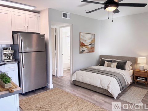 A bedroom with a bed, a refrigerator, and a ceiling fan.