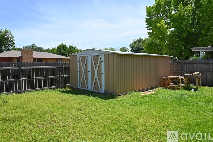 A shed with a brown roof and a white and brown design on the side is in a grassy yard.
