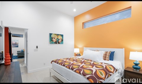 A bedroom with a bed, two lamps, and a painting on the wall.