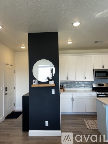 A kitchen with white cabinets and a black wall with a round mirror.
