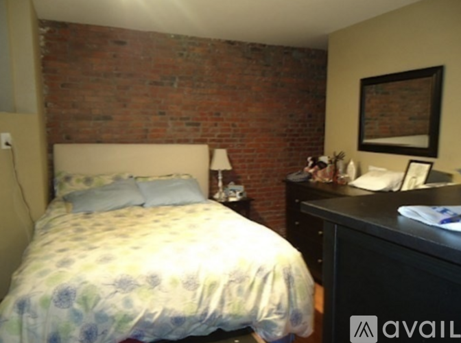 A bedroom with a brick wall and a bed with a floral comforter.