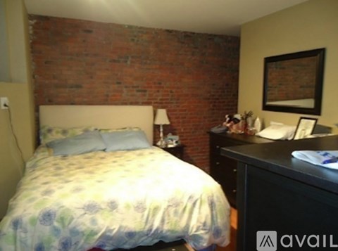 A bedroom with a brick wall and a bed with a floral comforter.