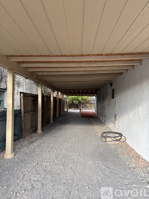 A long covered walkway with a white wall on one side and a gravel floor.