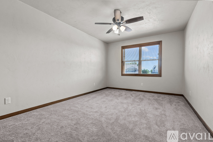 A room with a ceiling fan and a window overlooking a building.