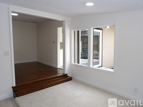 A room with a carpeted floor, wooden stairs, and a window with a view of a building outside.