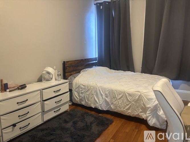 A bedroom with a white bed, white chair, and a black rug.
