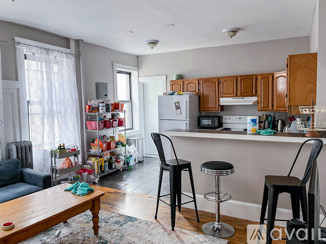 A kitchen with a refrigerator, microwave, and oven, with a bar stool and chair in front of it.