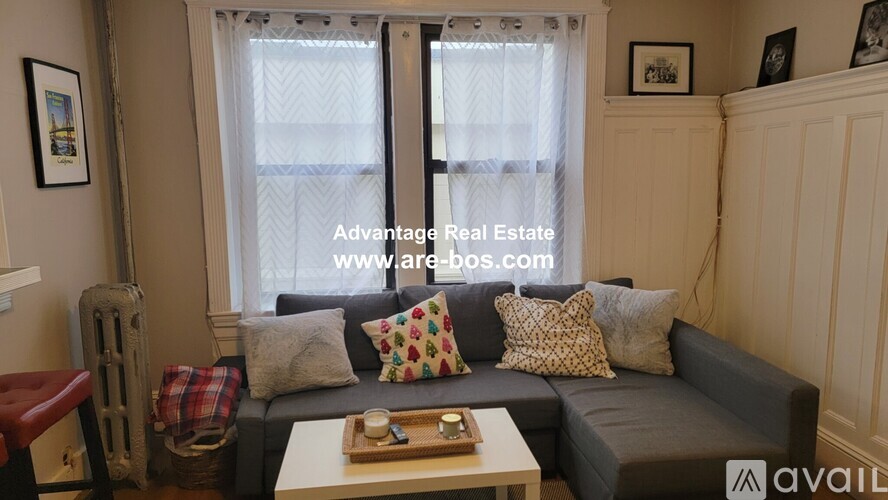 A living room with a grey couch, a wooden coffee table, and a window with curtains.