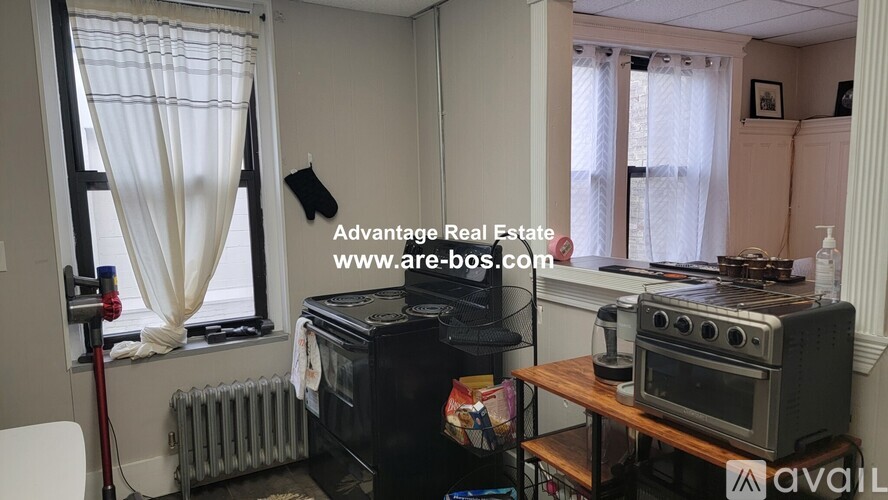 A small kitchen with a black stove and white curtains.